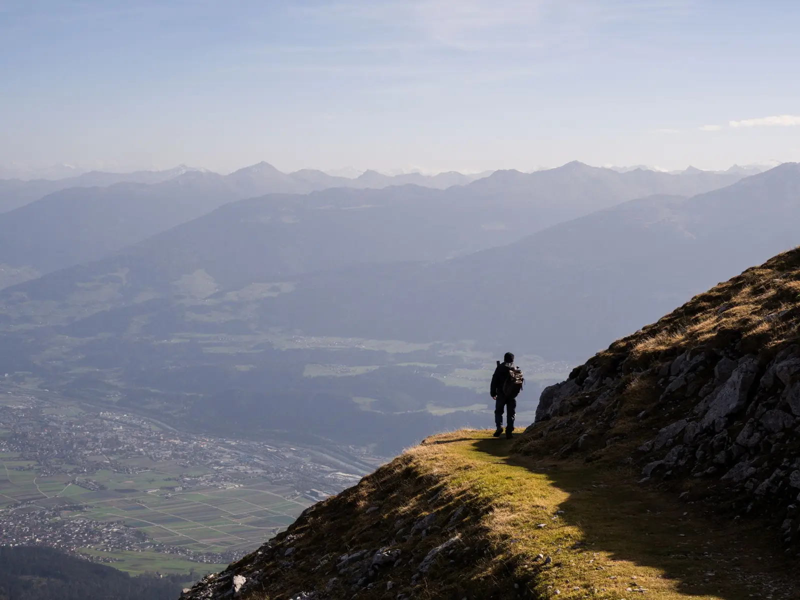 Hiker with a backpack standing on a grassy ridge above a wide mountain valley