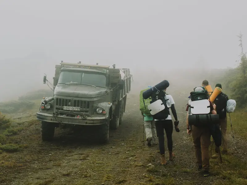 Hikers with loaded packs walking past an old truck on a foggy dirt road